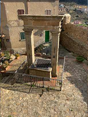 La foto mostra un pozzo sormontato da un arco in pietra e due colonne al centro.