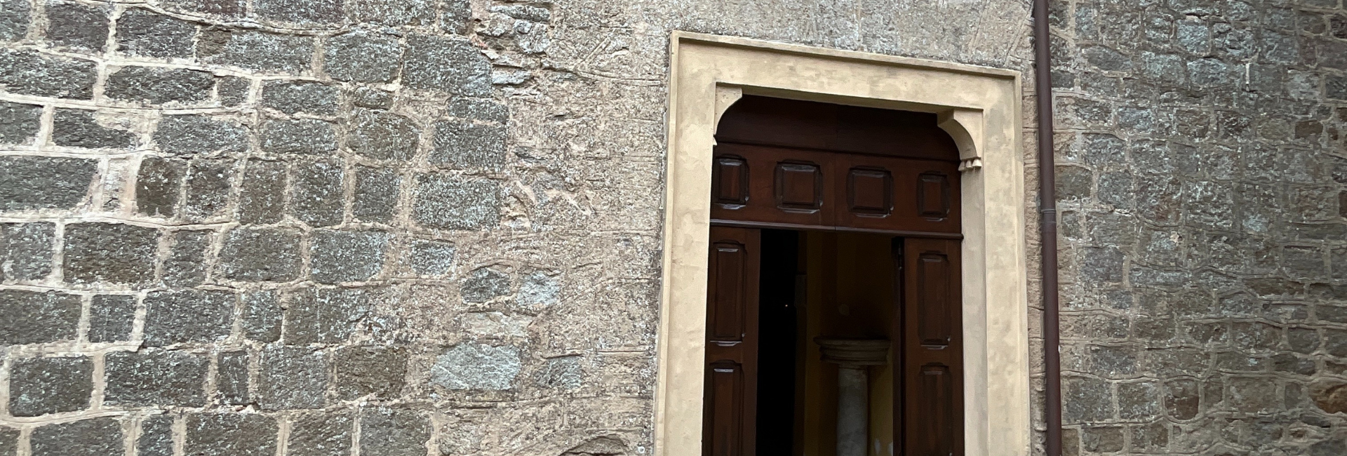 L'immagine rappresenta la porta in legno, aperta, ed il muro a sassi della chiesa.