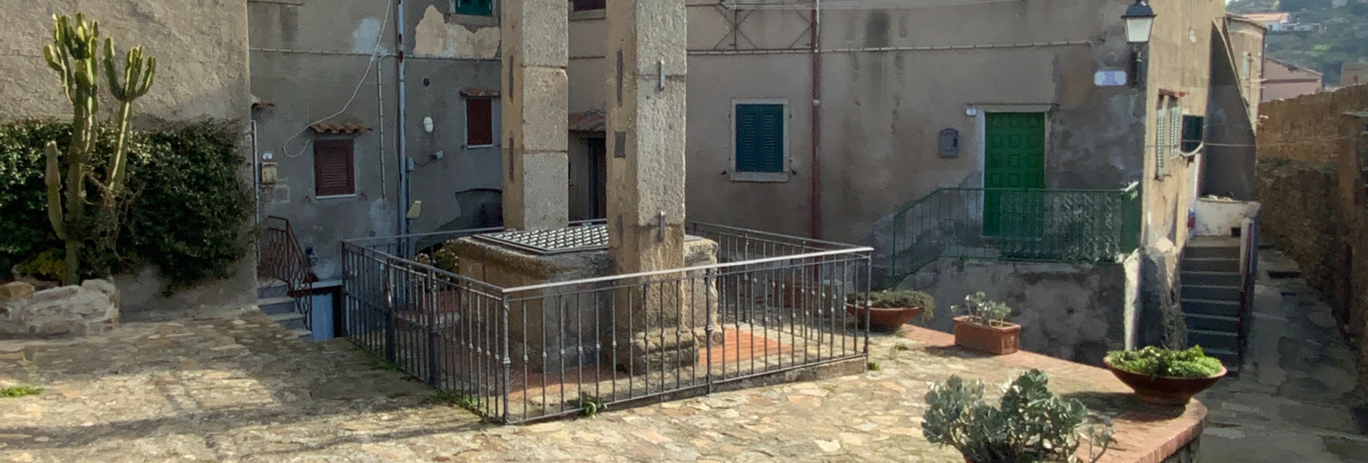 L'immagine mostra un cortile esterno lastricato in pietra, circondato da pareti in pietra. Al centro la cisterna.