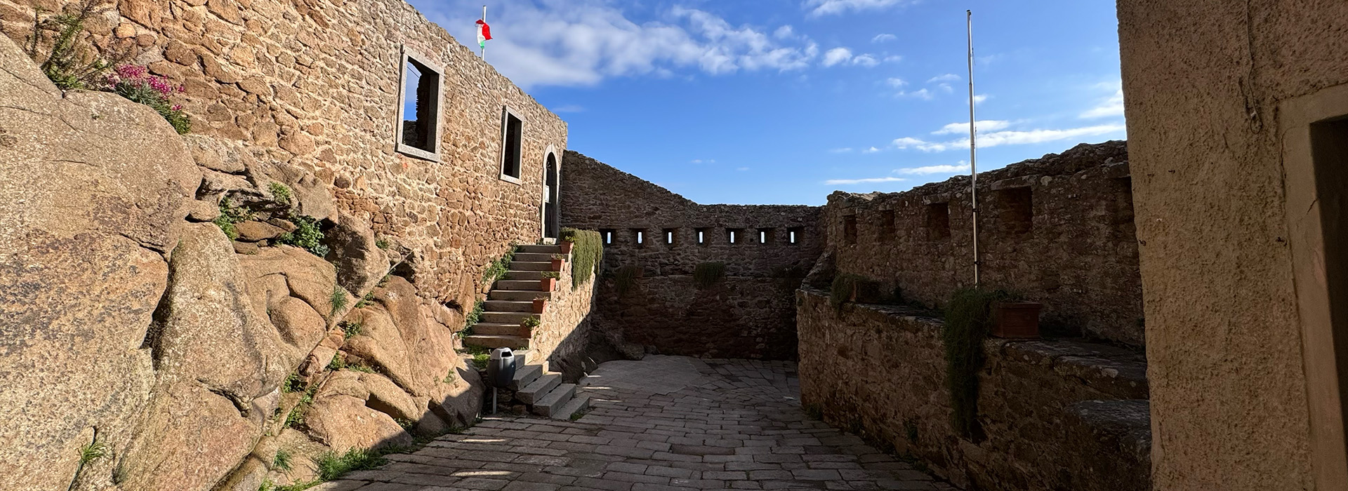 L'immagine mostra un cortile o un passaggio all'aperto, pavimentato con pietre.