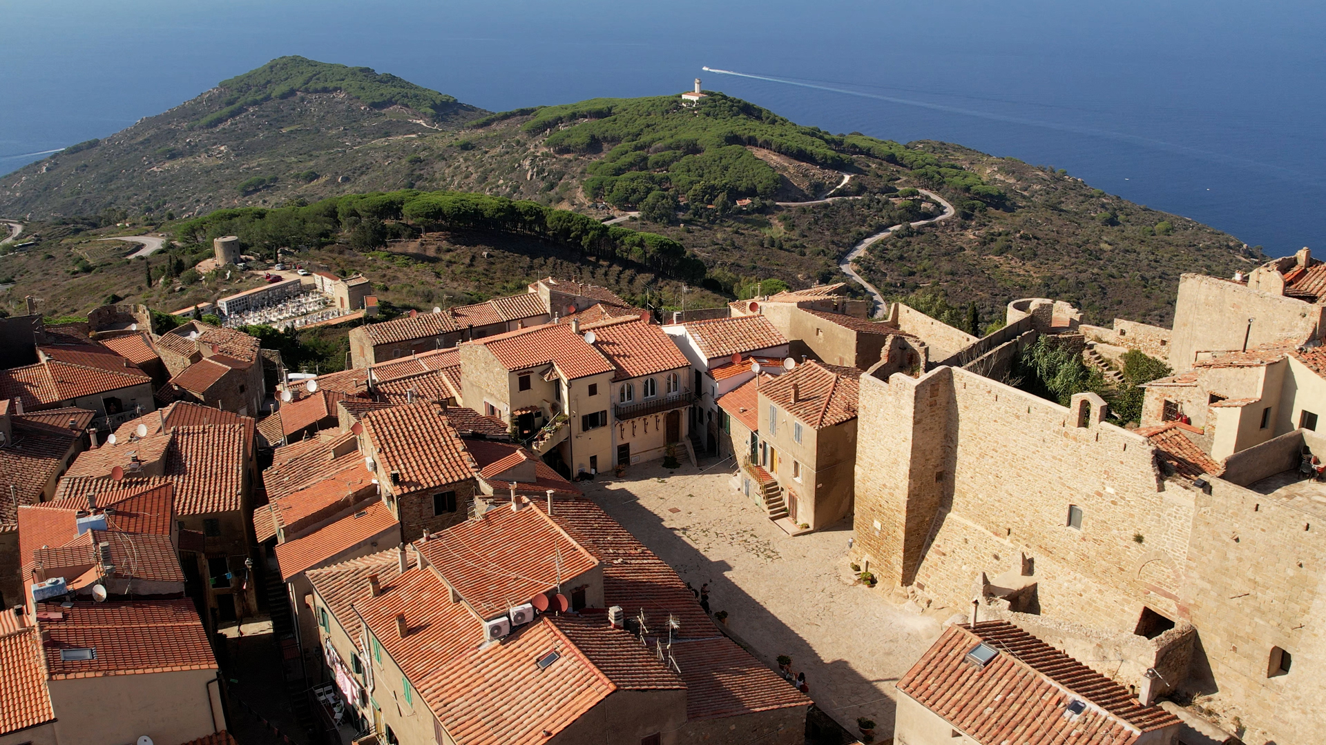 L'immagine mostra il borgo fortificato di Giglio Castello, sullo sfondo il faro e mare.