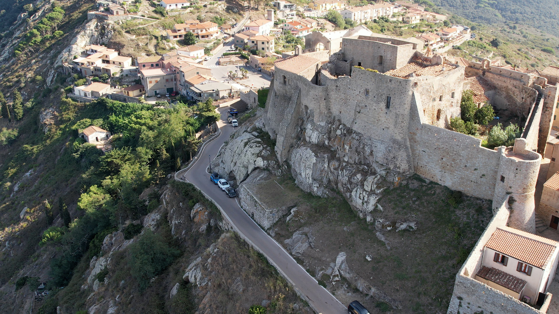 L'immagine mostra il borgo fortificato di Giglio Castello visto dall'alto. Rocca sulla destra e borgo sulla sinistra.