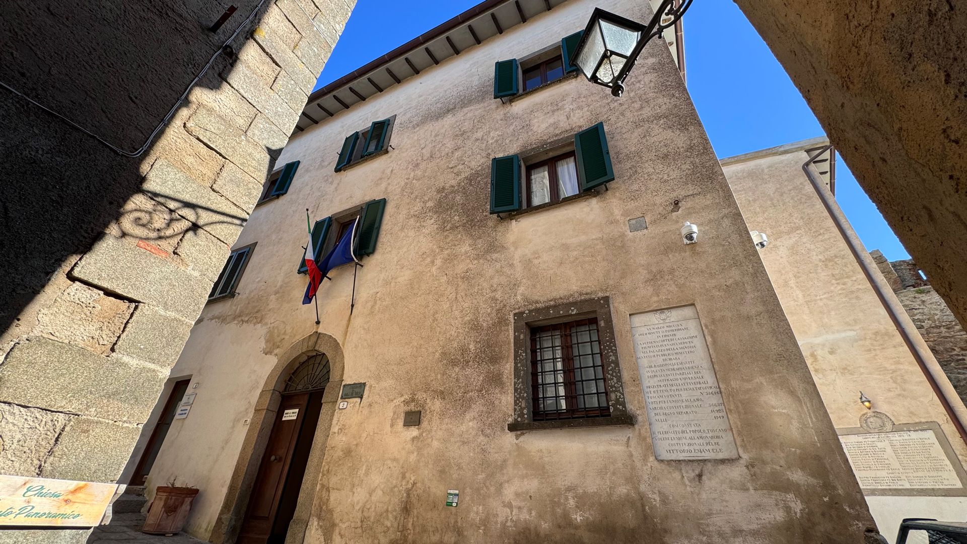 L'immagine mostra la facciata di un palazzo storico, il Municipio, visto dal basso lungo una strada in salita.