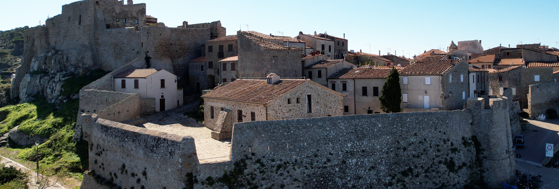 L'immagine mostra sulla sinistra c'è un'imponente fortezza in pietra, con alte mura grezze che si fondono con la roccia naturale.