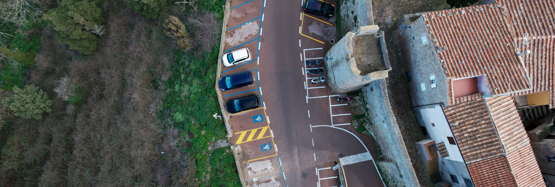 L'immagine è una vista aerea di una di porzione strada e parcheggio che che costeggiano un'antica cinta muraria.