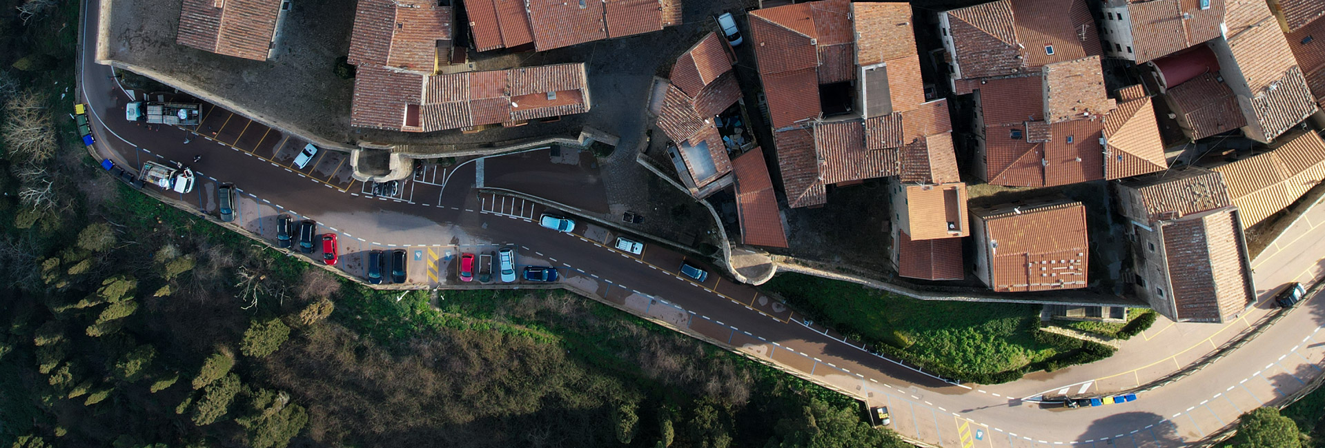 L'immagine è una veduta aerea di un antico borgo con una strada asfaltata che segue le mura.