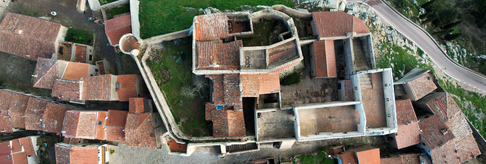 La foto, zenitale, mostra un complesso di edifici in pietra con tetti in tegole ed al centro la Rocca Pisana.