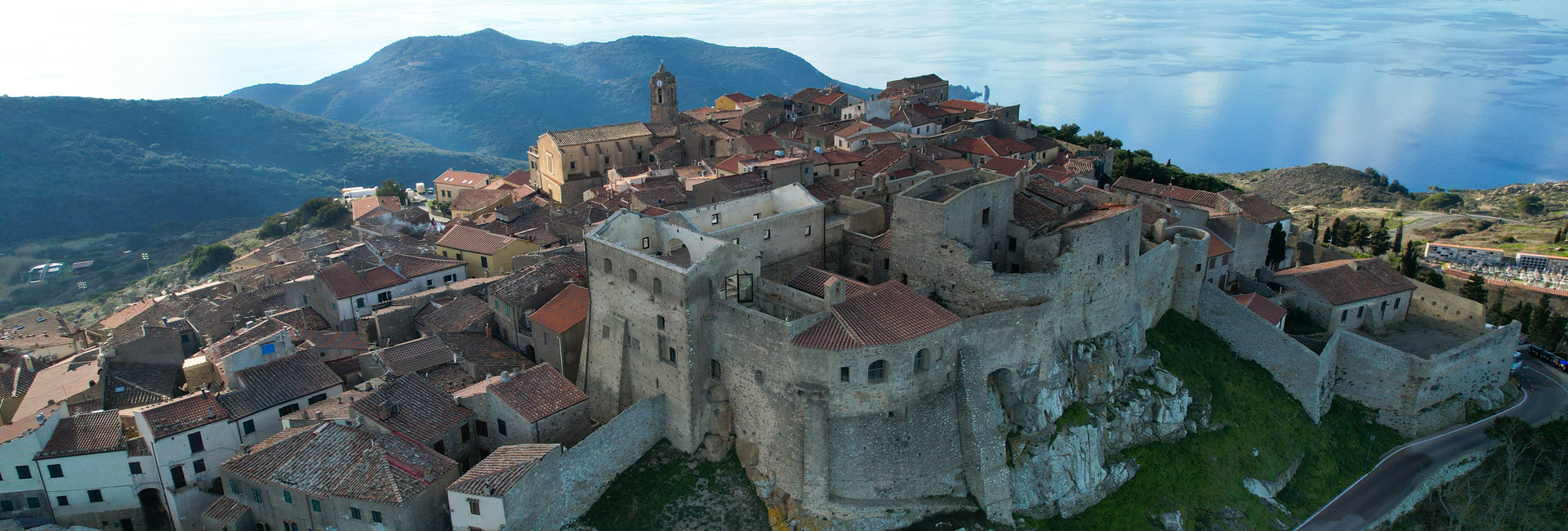 L'immagine mostra il borgo fortificato di Giglio Castello in una vista aerea che lo ritrae adagiato sulla cima di una collina.