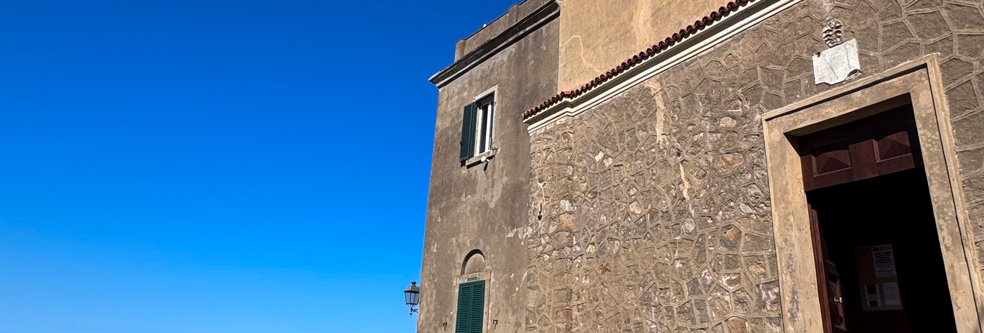 L'immagine mostra un edificio in muratura sulla destra con una facciata in pietra grezza.